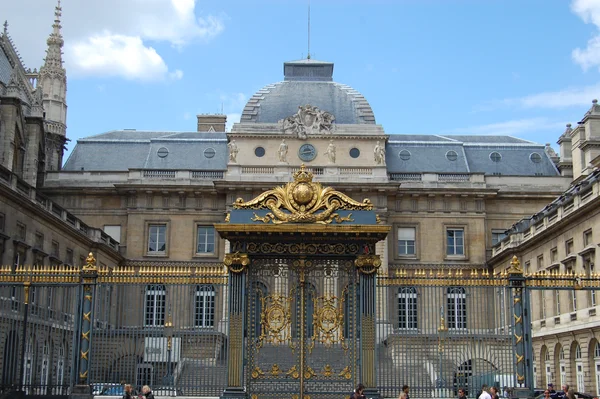 La porte dorée ornementale du Palais de Justice de Paris avec son architecture classique et son dôme visible sous un ciel bleu.