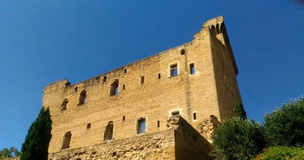 Photographie en plongée des murs crénelés et des fenêtres en arc du château médiéval de Châteauneuf-du-Pape contre un ciel bleu.