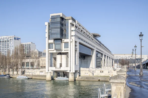 Immeuble du ministère de l'Économie et des Finances à Paris, bâtiment moderne de verre et de béton situé en bord de Seine avec des bateaux amarrés devant.
