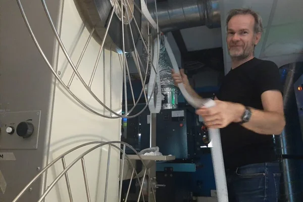 Technicien manipulant un flexible blanc dans une salle de projection 35 mm, entouré d'équipements industriels et de racks métalliques circulaires au cinéma Le Concorde à La Roche-sur-Yon.