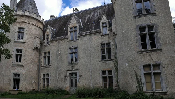 Façade extérieure du Château de Fougeret, le plus hanté de France, avec une tourelle ronde, des fenêtres à cadres de pierre et un toit d'ardoise sous un ciel nuageux.