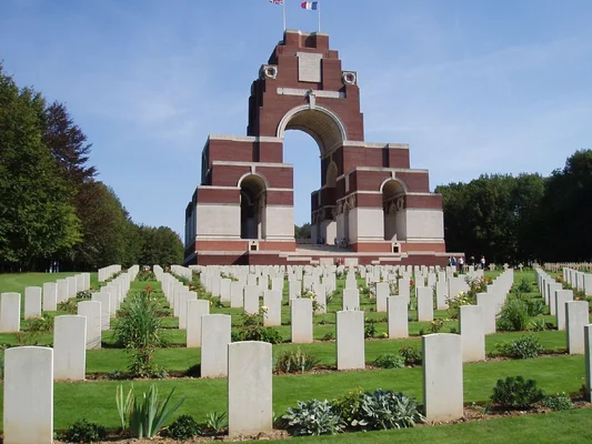 Le mémorial de Thiepval aux disparus de la Somme, un grand arc en brique et pierre surplombant des rangées de pierres tombales blanches dans un cimetière militaire sous un ciel bleu.