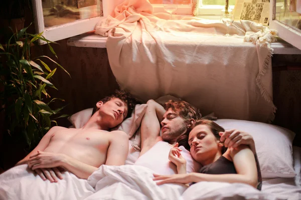 Trois personnes dormant ensemble dans un lit avec des draps blancs, symbole visuel d'un plan à trois réussi.
