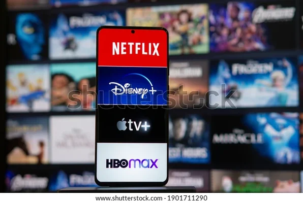 Un smartphone affichant les logos de Netflix, Disney+, Apple TV+ et HBO Max sur un fond flou de miniatures de films.