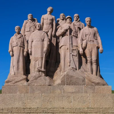 Monument en pierre de Paul Landowski représentant des soldats et des ouvriers, avec l'inscription 'LES FANTOMES' sur la base, sous un ciel bleu éclatant.