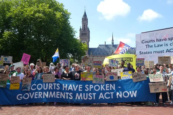Manifestants devant le Palais de la Paix à La Haye brandissant une bannière disant 'Les tribunaux ont parlé. Les gouvernements doivent agir maintenant' après l'avis consultatif de la CIJ sur le changement climatique.