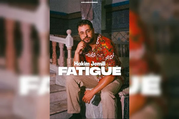 Hakim Jemili présentant son spectacle 'Fatigué' au Théâtre Édouard VII à Paris, scène éclairée, public attentif