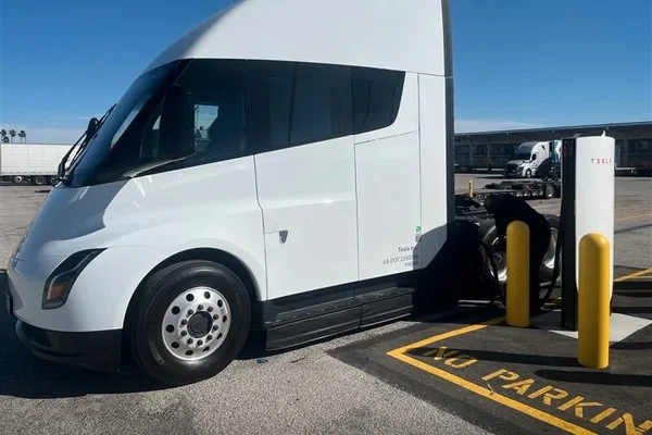 Tesla Semi blanc stationné à une borne Megacharger Tesla à Ontario, en Californie, avec une personne près des roues arrière et un marquage au sol jaune.