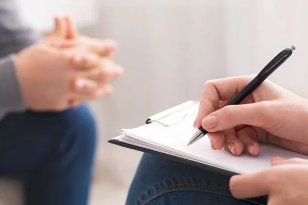 Mains tenues sur un cahier avec un stylo, écrivant lors d'une session de suivi psychologique, dans le cadre du dispositif Mon Soutien Psy