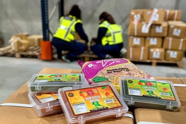 Bonbons Aam Papad saisis par les douaniers, présentés dans des boîtes en plastique dans un entrepôt, avec des employés en gilets haute visibilité en arrière-plan.