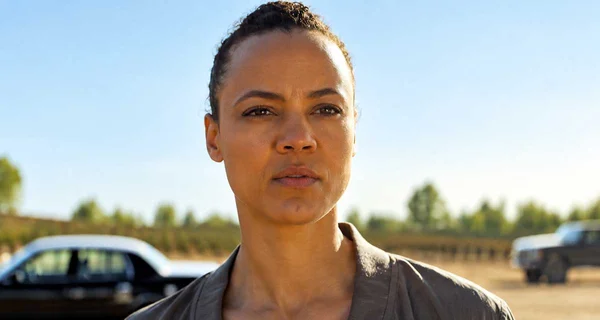 Maria Sten, cheveux sombres attachés en arrière, portant un haut gris, regarde fixement la caméra avec une expression sérieuse, sur un fond flou extérieur avec des véhicules, dans le spin-off Neagley de Reacher sur Prime Video