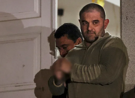 Cédric Prizzon, suspect dans l'affaire des disparues de l'Aveyron, vêtu d'une veste verte, regardant la caméra devant une porte blanche, accompagné d'un autre homme.