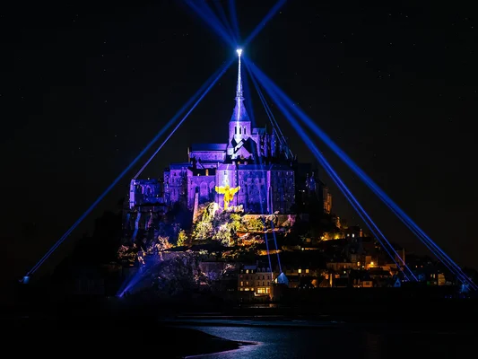 Mont-Saint-Michel vu depuis une perspective aérienne ou panoramique montrant l'abbaye médievale et le village entourés d'eau et de lumières chaudes