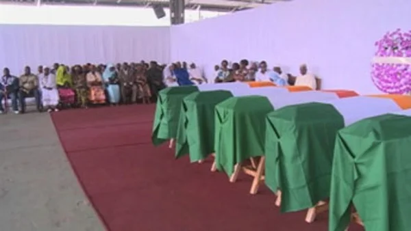 Cercueils recouverts des drapeaux ivoiriens verts, blancs et orange alignés sur un tapis rouge lors de la remise symbolique des corps de victimes de la crise ivoirienne à leurs familles, avec des proches endeuillés assis en arrière-plan.