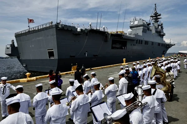 Destroyer de la marine japonaise amarré au port de Manille aux Philippines le 21 juin, avec des marins en uniforme blanc jouant des cuivres sur le quai devant le grand navire gris battant pavillon japonais