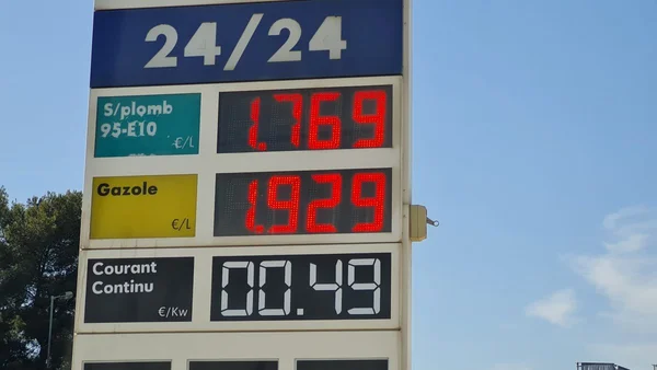Panneau de prix d'une station-essence affichant le sans-plomb 95-E10, le gazole à 1,929 euro le litre et la recharge en courant continu sous un ciel bleu