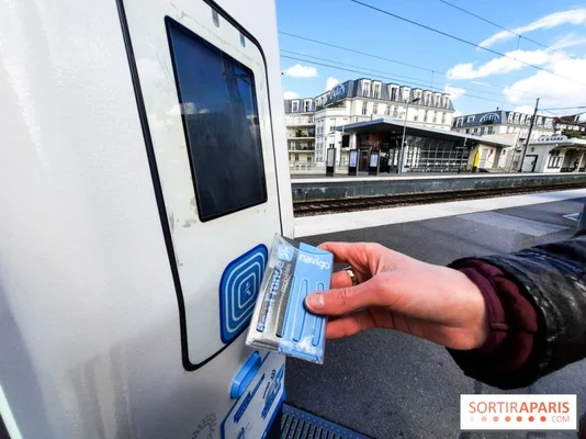 Main d'un voyageur validant un pass Navigo bleu sur le lecteur d'un tourniquet d'accès sur un quai de gare parisienne en extérieur