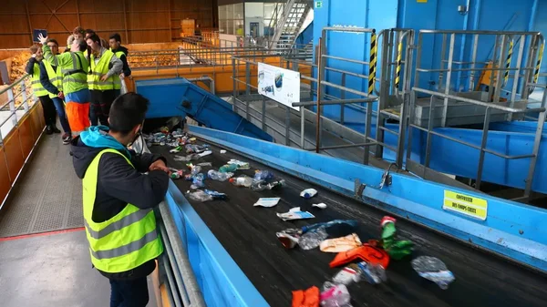 Des visiteurs portant des gilets de sécurité jaunes observent des matériaux en décomposition sur un tapis roulant dans un centre de tri industriel.