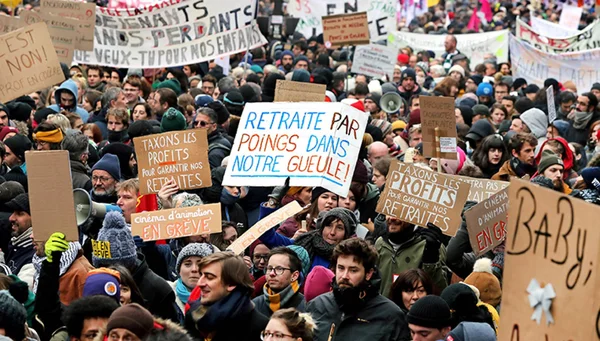 Foule dense de manifestants marchant en extérieur lors de la mobilisation massive contre la réforme des retraites, tenant des pancartes artisanales sur les retraites et les profits