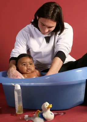 Photographie montrant Lionel Messi, âgé de 20 ans, lavant le bébé Lamine Yamal dans un bain bleu en plastique contre un fond rouge, avec une bouteille de savon et un canard en caoutchouc, lors d'une séance photo caritative en 2007.