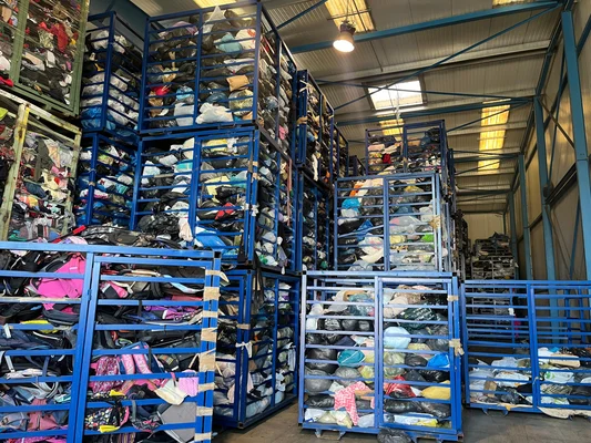 Intérieur d'un entrepôt rempli de rangées bleu métalliques contenant des sacs de vêtements et de textiles en surabondance, illustrant la crise de la filière de recyclage.