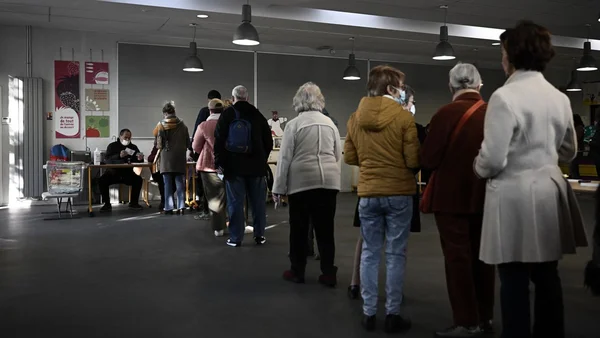 Assesseurs veillant au bon déroulé du scrutin lors de l'élection présidentielle, avec des files d'attente d'électeurs devant les bureaux de vote