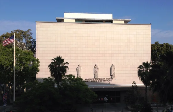 Le palais de justice Stanley Mosk à Los Angeles, grande façade en pierre claire surmontée de trois statues au-dessus de l'entrée, entourée d'arbres avec un drapeau américain en journée