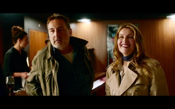 Gilles Lellouche et Laetitia Casta dans « Le Crime du 3e étage » : lui en veste verte sur une chemise sombre, elle en trench beige, souriants dans un décor de restaurant.