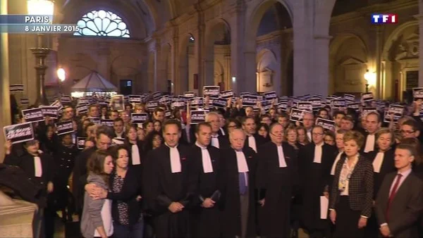 Groupe de personnes, dont de nombreux magistrats et avocats en robe noire, rassemblées debout dans un couloir du Palais de justice de Paris et brandissant des pancartes « Je suis Charlie »