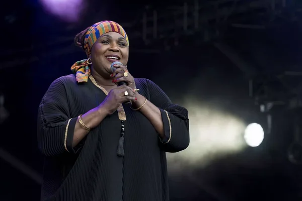 Bibie chantant en micro sur scène, vêtue d'un foulard coloré et d'un haut noir à plis avec bordures dorées, lors d'un événement entre la France et le Ghana.