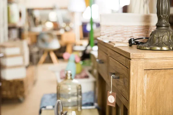 Gros plan d'un meuble en bois avec tiroirs exposé dans une boutique d'objets et meubles d'occasion Emmaüs, avec un objet en laiton décoratif sur le dessus et un fond flou de l'intérieur du magasin.