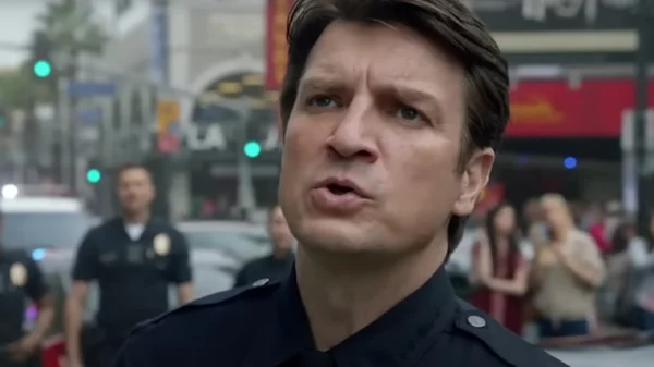 Nathan Fillion en tenue d'officier de police debout dans la rue, parlant à l'extérieur sur une rue de ville avec d'autres officiers et piétons visibles en arrière-plan flou.