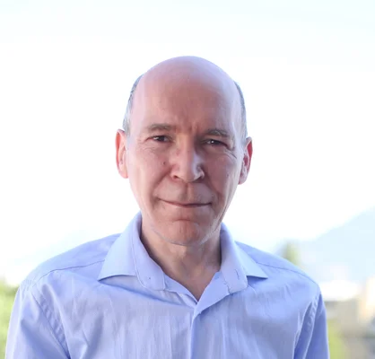Étienne Cunge, auteur de « La Rep », portrait rapproché en chemise bleu clair, souriant légèrement devant un arrière-plan extérieur lumineux et flou.