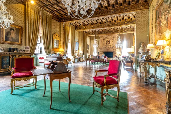 Salon d'apparat du château de Brissac avec fauteuils en velours rouge, bureau en bois, lustres, parquet et tapisseries