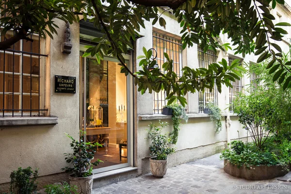 Devanture de la boutique Richard Orfèvre à Paris, avec de grandes vitrines exposant des bijoux, encadrée par des plantes vertes et des arbres.