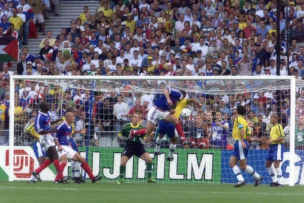 Zinédine Zidane lors de la finale de la Coupe du monde 1998, action disputée près du filet avec le gardien en vert devant le but et une foule nombreuse en tribunes