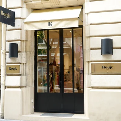 Façade de la boutique Rouje à Paris, 2 rue Bachaumont, avec porte vitrée à encadrement sombre, auvent crème orné d'un R et plaques Rouje Paris sur pierre claire