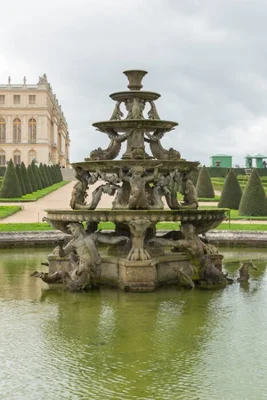 La fontaine de la Pyramide de François Girardon, vasque en pierre sculptée à plusieurs niveaux au centre d'un bassin aux eaux vertes, avec le palais classique et des topiaires taillées en arrière-plan dans les jardins de Versailles