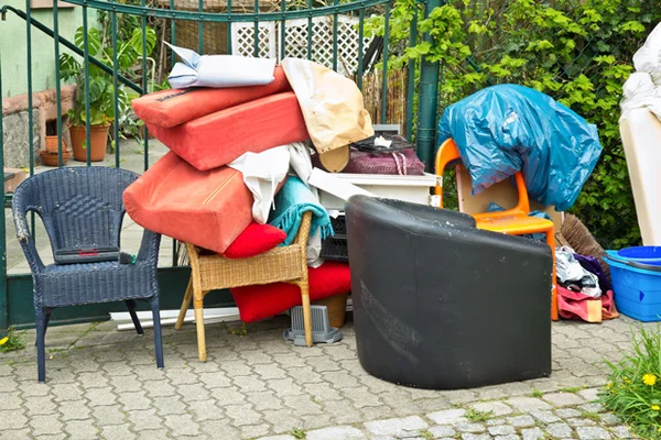 Tas de meubles et objets encombrants abandonnés, chaises, coussins et sacs entassés sur une terrasse pavée près d'une clôture à Bron