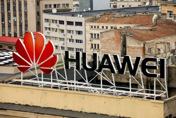 Grande enseigne Huawei avec logo rouge en fleur et lettres noires sur le toit d'un immeuble, avec en arrière-plan des bâtiments anciens et des antennes paraboliques