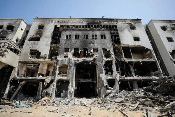 Le bâtiment chirurgical d'un hôpital de Gaza détruit, aux fenêtres soufflées, étages exposés et traces de brûlure, avec des tas de gravats au premier plan sous un ciel dégagé