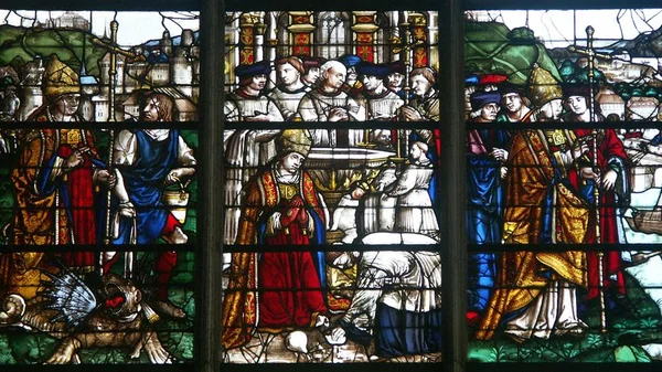 Vitrail en trois panneaux aux scènes colorées représentant saint Romain et des figures religieuses en robes, la bête mythique de la Gargouille de Rouen en bas à gauche et des décors architecturaux en arrière-plan