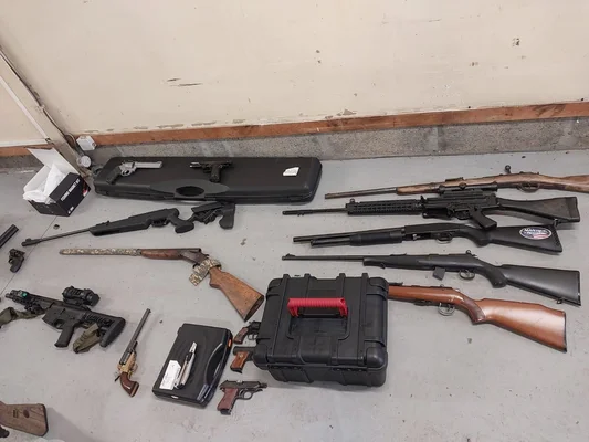 Assortiment de fusils, carabines et armes de poing saisis près de Rouen, alignés sur un sol en béton avec étuis et accessoires après la saisie de 47 armes et 300 kg de munitions