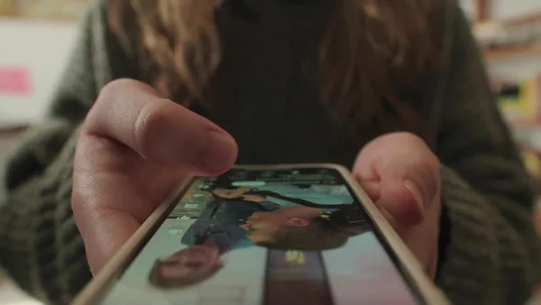 Gros plan sur les mains d'une personne faisant défiler un fil d'actualité sur son smartphone