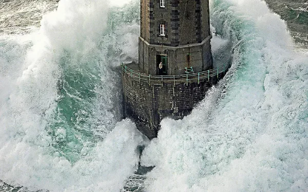 Le phare de la Jument à Ouessant, tour en pierre tenant bon tandis que d'immenses vagues blanches s'écrasent violemment contre sa base en pleine tempête