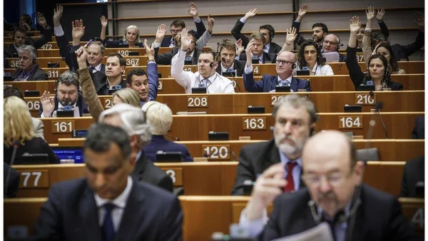 Des eurodéputés levant la main pour voter lors d'une mini-session plénière à Bruxelles, assis derrière des pupitres numérotés en gradins dans l'hémicycle
