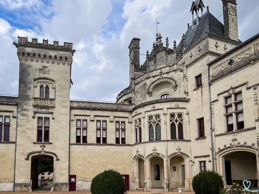 Cour intérieure du château de Brézé avec murs en pierre claire, fenêtres à remplage gothique, tour carrée crénelée et passages voûtés sous un ciel nuageux