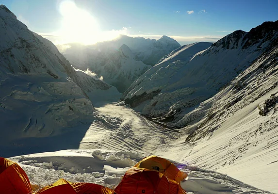 Tentes d'expédition orange installées sur la neige au camp 3 sur la face du Lhotse, surplombant une vaste vallée glaciaire ensoleillée bordée de sommets enneigés sous un ciel bleu limpide