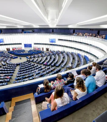 Vue intérieure large de l'hémicycle du Parlement européen à Strasbourg en session plénière, avec rangées de sièges bleus, drapeaux nationaux et européen, public en tribune