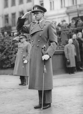 Le roi Baudouin de Belgique en uniforme militaire et manteau long, saluant avec une épée lors de la cérémonie du Armistice à Bruxelles, le 12 novembre 1956. D’autres figures sont visibles en arrière-plan.